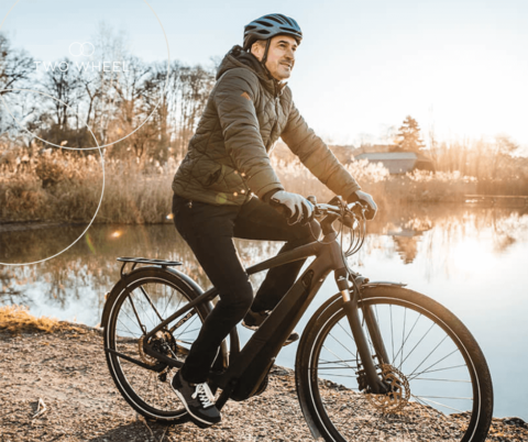 Mandlig cyklist på vej på arbejde, cykler langs sø oplyst af morgensolen